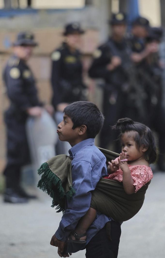 A boy carrying a child stands in front of police officers at a site where a man had been lynched in Tactic, in Alta Verapaz region, some 189 km (117 miles) from Guatemala City, September 12, 2012. According to local media, the man who was lynched and burnt alive by a mob, had entered a school and killed two children, 8-year-old and a 13-year-old, with a machete. REUTERS/Jorge Dan Lopez (GUATEMALA - Tags: EDUCATION CRIME LAW) Published: Zář. 13, 2012, 1:34 dop.