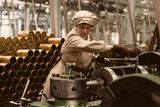 Žena ve zbrojní továrně ve Velké Británii kompletuje dělostřelecký granát, aby měli vojáci na frontě s čím bojovat proti nepříteli. Náročnou práci v muničních továrnách za první světové války běžně vykonávaly ženy. Někdy se jim přezdívalo "canaries" ("kanárkové dívky"), protože měly kvůli síře zažloutlou kůži. Ve zbrojovkách panovaly velmi špatné pracovní a bezpečnostní podmínky, které měly za následek smrt stovek lidí.