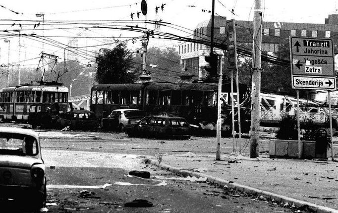 Ohořelé zbytky aut a tramvají stojí na křižovatce v centru Sarajeva po zásahu dělostřeleckou palbou. Květen 1992.