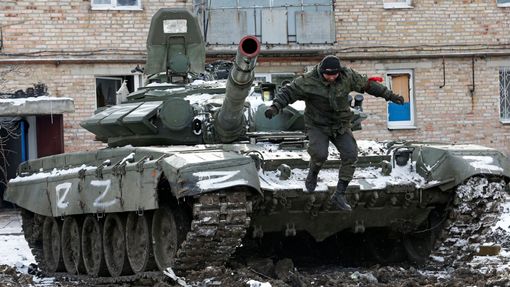 Proruský separatista seskakuje z tanku s písmenem Z u rozbombardovaného domu ve městě Volnovacha.