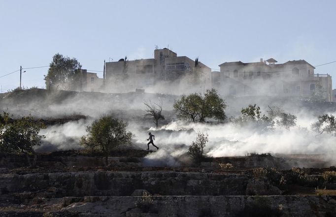 A Palestinian stone-thrower runs after Israeli security forces fired tear gas during clashes against Israel's military operation in Gaza, outside Ofer prison near the West Bank city of Ramallah November 15, 2012. A rocket fired from the Gaza Strip landed close to Tel Aviv on Thursday, in the first attack on Israel's biggest city in 20 years, raising the stakes in a military showdown between Israel and the Palestinians that is moving towards all-out war. REUTERS/Mohamad Torokman (WEST BANK - Tags: POLITICS CIVIL UNREST) Published: Lis. 15, 2012, 6:22 odp.