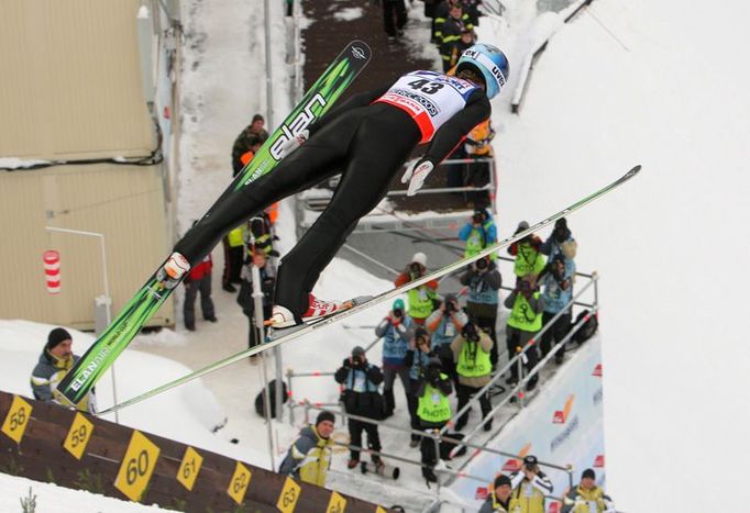 Jakub Janda letí nad tribunou pro fotografy v kvalifikaci na závod mužů na můstku HS-100.