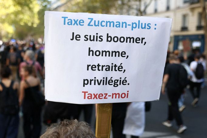 Protestující drží transparent s nápisem „Zdanit Zucman-plus, jsem boomer, muž, důchodce, privilegovaný. Zdaníte mě“ během demonstrace v Paříži.