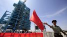 A soldier gestures in front of the launch pad holding the Long March II-F rocket loaded with the Shenzhou-9 manned spacecraft, in Jiuquan Satellite Launch Center, Gansu province, June 16, 2012. China will send its first woman into outer space this week, prompting a surge of national pride as the rising power takes its latest step towards putting a space station in orbit within the decade. Liu Yang, a 33-year-old fighter pilot, will join two other astronauts aboard the Shenzhou 9 spacecraft when it lifts off from a remote Gobi Desert launch site on Saturday evening. REUTERS/Jason Lee (CHINA - Tags: MILITARY SCIENCE TECHNOLOGY) Published: Čer. 16, 2012, 5:08 dop.