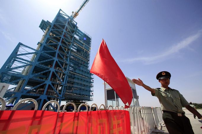 A soldier gestures in front of the launch pad holding the Long March II-F rocket loaded with the Shenzhou-9 manned spacecraft, in Jiuquan Satellite Launch Center, Gansu province, June 16, 2012. China will send its first woman into outer space this week, prompting a surge of national pride as the rising power takes its latest step towards putting a space station in orbit within the decade. Liu Yang, a 33-year-old fighter pilot, will join two other astronauts aboard the Shenzhou 9 spacecraft when it lifts off from a remote Gobi Desert launch site on Saturday evening. REUTERS/Jason Lee (CHINA - Tags: MILITARY SCIENCE TECHNOLOGY) Published: Čer. 16, 2012, 5:08 dop.