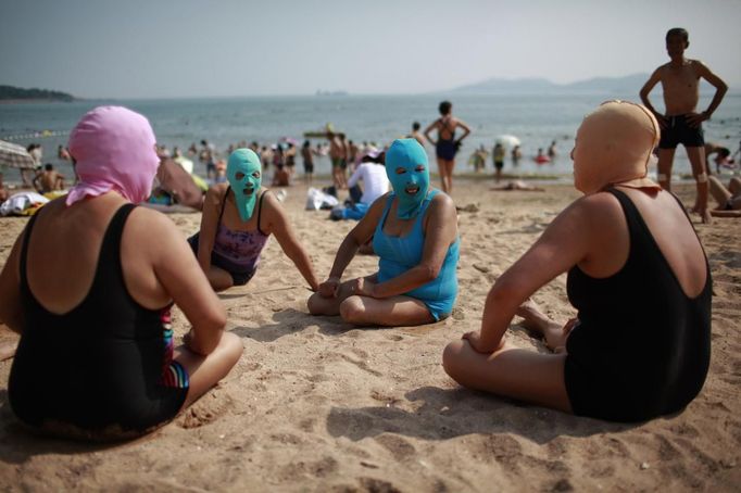 Women, wearing nylon masks, chat as they rest on the shore during their visit to a beach in Qingdao, Shandong province July 6, 2012. The mask, which was invented by a woman about seven years ago, is used to block the sun's rays. The mask is under mass production and is on sale at local swimwear stores. REUTERS/Aly Song (CHINA - Tags: SOCIETY TRAVEL ENVIRONMENT) Published: Čec. 6, 2012, 4:31 odp.