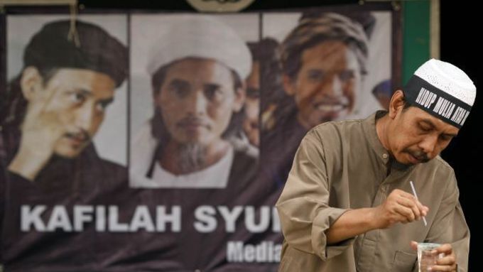 Jeden ze sympatizantů odsouzených teroristů stojí před plakátem s jejich tvářemi.