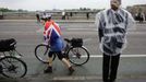 OLY-WEATHER-CONTINGENCY/ Description: A guard uses a plastic jacket to protect himself from rain, next to a cyclist draped with the Union Flag, on Putney Bridge in London in this June 3, 2012 file photo. A quarter of a million rain ponchos, an army of volunteers equipped with umbrellas and rain jackets, and five dedicated weather forecasters - it must be a British Olympics. Planning any outdoor event during the unpredictable British summer, renowned for its potential to throw up more rainy spells than sunshine, requires drawing up contingency plans and keeping a close eye on the weather. REUTERS/Kevin Coombs/Files (BRITAIN - Tags: SOCIETY SPORT OLYMPICS ENVIRONMENT) Published: Čer. 27, 2012, 6:49 dop.