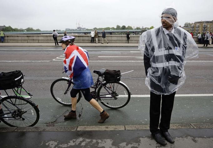 OLY-WEATHER-CONTINGENCY/ Description: A guard uses a plastic jacket to protect himself from rain, next to a cyclist draped with the Union Flag, on Putney Bridge in London in this June 3, 2012 file photo. A quarter of a million rain ponchos, an army of volunteers equipped with umbrellas and rain jackets, and five dedicated weather forecasters - it must be a British Olympics. Planning any outdoor event during the unpredictable British summer, renowned for its potential to throw up more rainy spells than sunshine, requires drawing up contingency plans and keeping a close eye on the weather. REUTERS/Kevin Coombs/Files (BRITAIN - Tags: SOCIETY SPORT OLYMPICS ENVIRONMENT) Published: Čer. 27, 2012, 6:49 dop.