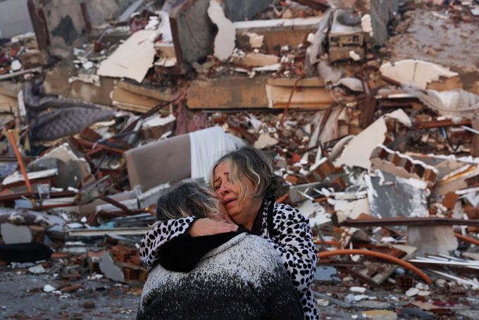Žena reaguje při objímání jiné osoby v blízkosti trosek po zemětřesení v tureckém městě Hatay,