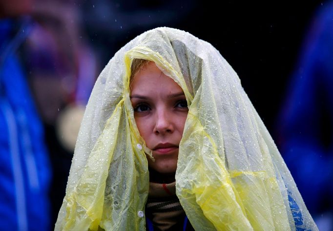 A spectator uses a raincover to protect herself from rain as she waits for the start of s