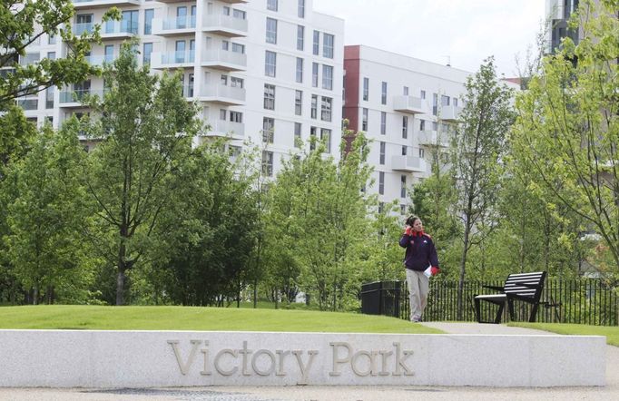 A LOCOG (London Organising Committee of the Olympic Games) employee crosses Victory Park in the Olympic Village built for the London 2012 Olympic Games in Stratford, east London on June 29, 2012. The village will accomodate up to 16,000 athletes and officials from more than 200 nations. Picture taken June 29, 2012. REUTERS/Olivia Harris (BRITAIN - Tags: BUSINESS CONSTRUCTION SPORT OLYMPICS CITYSPACE) Published: Čer. 30, 2012, 12:21 odp.