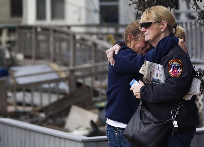 People embrace after looking through the wreckage of homes devastated by fire and the affects of Hurricane Sandy in the Breezy Point section of the Queens borough of New York October 31, 2012. The U.S. Northeast began an arduous slog back to normal on Wednesday after historic monster storm Sandy crippled transportation, knocked out power for millions and killed at least 64 people with a massive storm surge that caused epic flooding. REUTERS/Shannon Stapleton (UNITED STATES - Tags: ENVIRONMENT DISASTER) Published: Říj. 31, 2012, 8:32 odp.