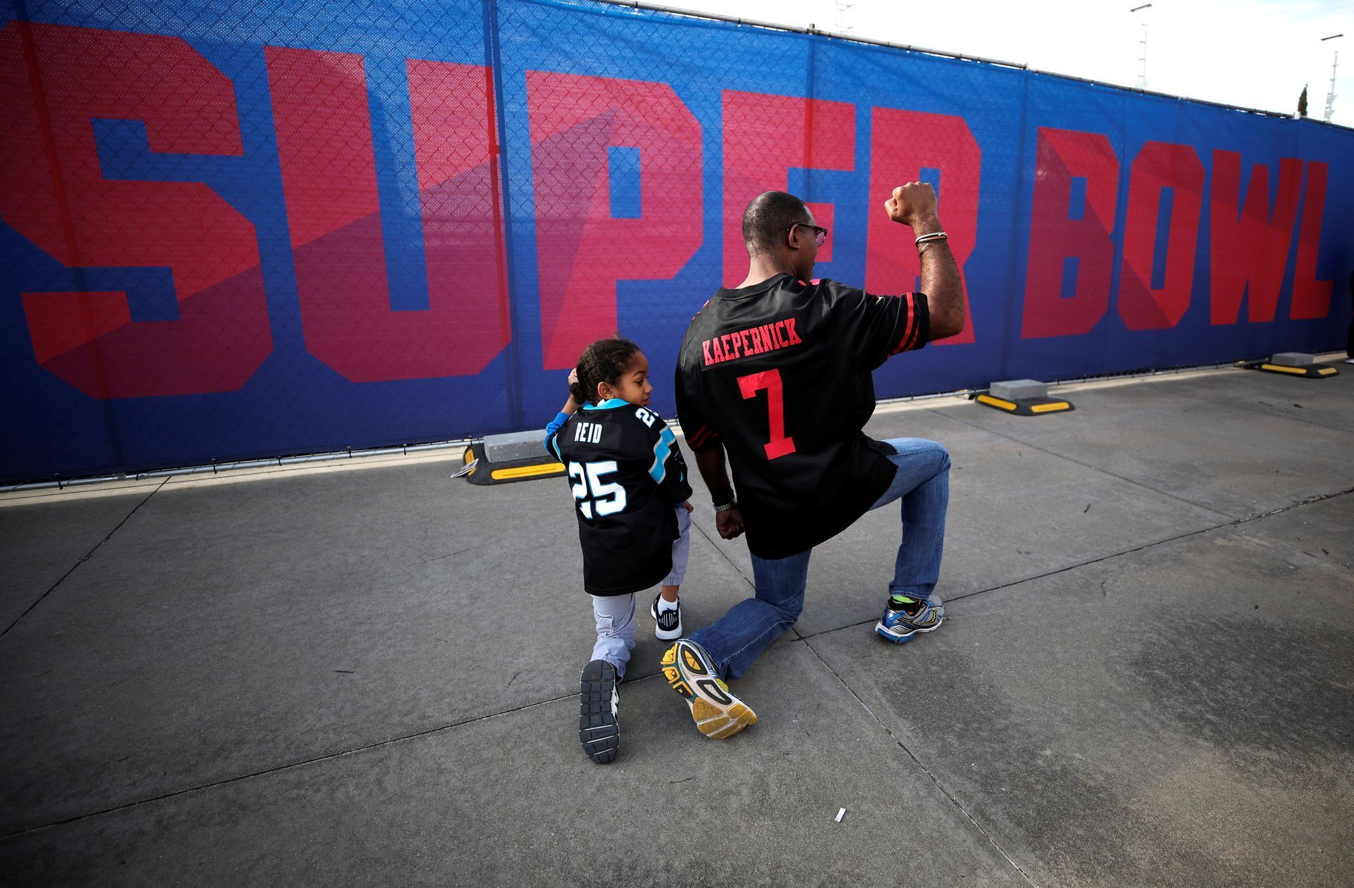 Fanoušek amerického fotbalu a jeho syn napodobuje gesto Colina Kaepernicka, jednoho z "klečících fotbalistů", na jeho podporu