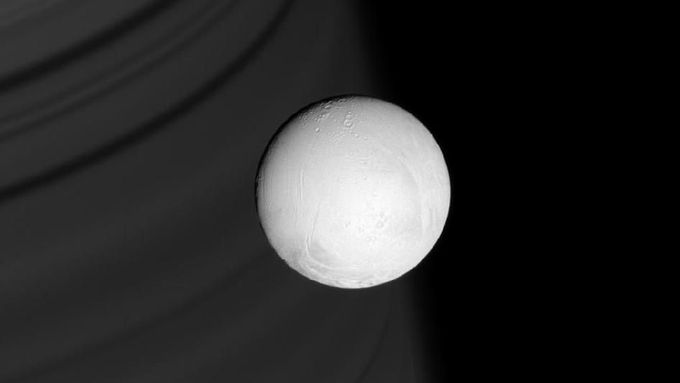 Enceladus ze vzdálenosti 291 000 kilometrů. V pozadí Saturn.