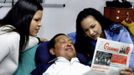 Venezuela's President Hugo Chavez holds a copy of the newspapers as his daughters, Rosa Virginia (R) and Maria watch while recovering from cancer surgery in Havana in this photograph released by the Ministry of Information on February 15, 2013. Venezuela's government published the first pictures of cancer-stricken Chavez since his operation in Cuba more than two months ago, showing him smiling while lying in bed reading a newspaper, flanked by his two daughters. The 58-year-old socialist leader had not been seen in public since the Dec. 11 surgery, his fourth operation in less than 18 months. The government said the photos were taken in Havana on February 14, 2013. REUTERS/Ministry of Information/Handout (VENEZUELA - Tags: POLITICS PROFILE HEALTH) ATTENTION EDITORS - THIS IMAGE WAS PROVIDED BY A THIRD PARTY. FOR EDITORIAL USE ONLY. NOT FOR SALE FOR MARKETING OR ADVERTISING CAMPAIGNS. THIS PICTURE IS DISTRIBUTED EXACTLY AS RECEIVED BY REUTERS, AS A SERVICE TO CLIENTS Published: Úno. 15, 2013, 3:25 odp.