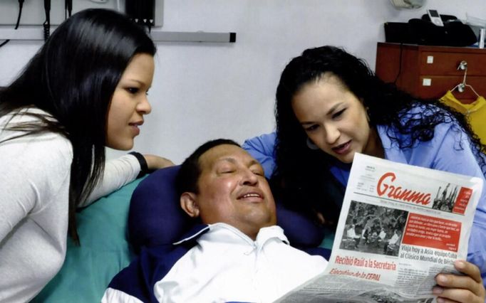 Venezuela's President Hugo Chavez holds a copy of the newspapers as his daughters, Rosa Virginia (R) and Maria watch while recovering from cancer surgery in Havana in this photograph released by the Ministry of Information on February 15, 2013. Venezuela's government published the first pictures of cancer-stricken Chavez since his operation in Cuba more than two months ago, showing him smiling while lying in bed reading a newspaper, flanked by his two daughters. The 58-year-old socialist leader had not been seen in public since the Dec. 11 surgery, his fourth operation in less than 18 months. The government said the photos were taken in Havana on February 14, 2013. REUTERS/Ministry of Information/Handout (VENEZUELA - Tags: POLITICS PROFILE HEALTH) ATTENTION EDITORS - THIS IMAGE WAS PROVIDED BY A THIRD PARTY. FOR EDITORIAL USE ONLY. NOT FOR SALE FOR MARKETING OR ADVERTISING CAMPAIGNS. THIS PICTURE IS DISTRIBUTED EXACTLY AS RECEIVED BY REUTERS, AS A SERVICE TO CLIENTS Published: Úno. 15, 2013, 3:25 odp.