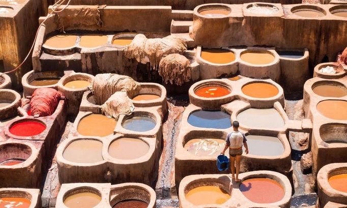 Muž s kbelíkem mezi tradičními kamennými káděmi s přírodními barvivy, kde se zpracovávají zvířecí kůže. Chouara Tannery, Fez, Maroko, 7. května 2017