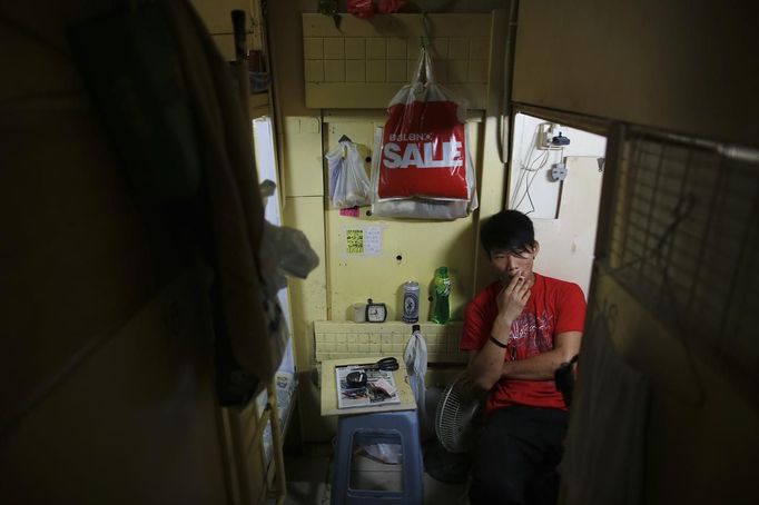 King, 18, who works as a bartender smokes his cigarette in a wooden box he uses as living space in Hong Kong October 9, 2012. In Hong Kong's middle-class residential area, short distance from its shopping and financial districts, 24 people live in these wooden boxes, or "coffin homes", packed in a single apartment of little over 50 square meters. Its residents pay 1450 Hong Kong dollars ($180) for their living space built of wooden panels of 2 meters by 70 cm. To maximize income from the rent in central Hong Kong landlords build "coffin homes", nicknamed due to their resemblance to real coffins. Space has always been at a premium in Hong Kong where developers plant high-rises on every available inch. REUTERS/Damir Sagolj (CHINA - Tags: SOCIETY REAL ESTATE BUSINESS) Published: Říj. 9, 2012, 1:45 odp.