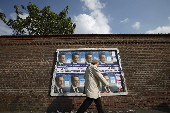 A local resident walks past a wall posted with posters in support of Sarkozy, France's President and UMP party candidate for the 2012 French presidential election