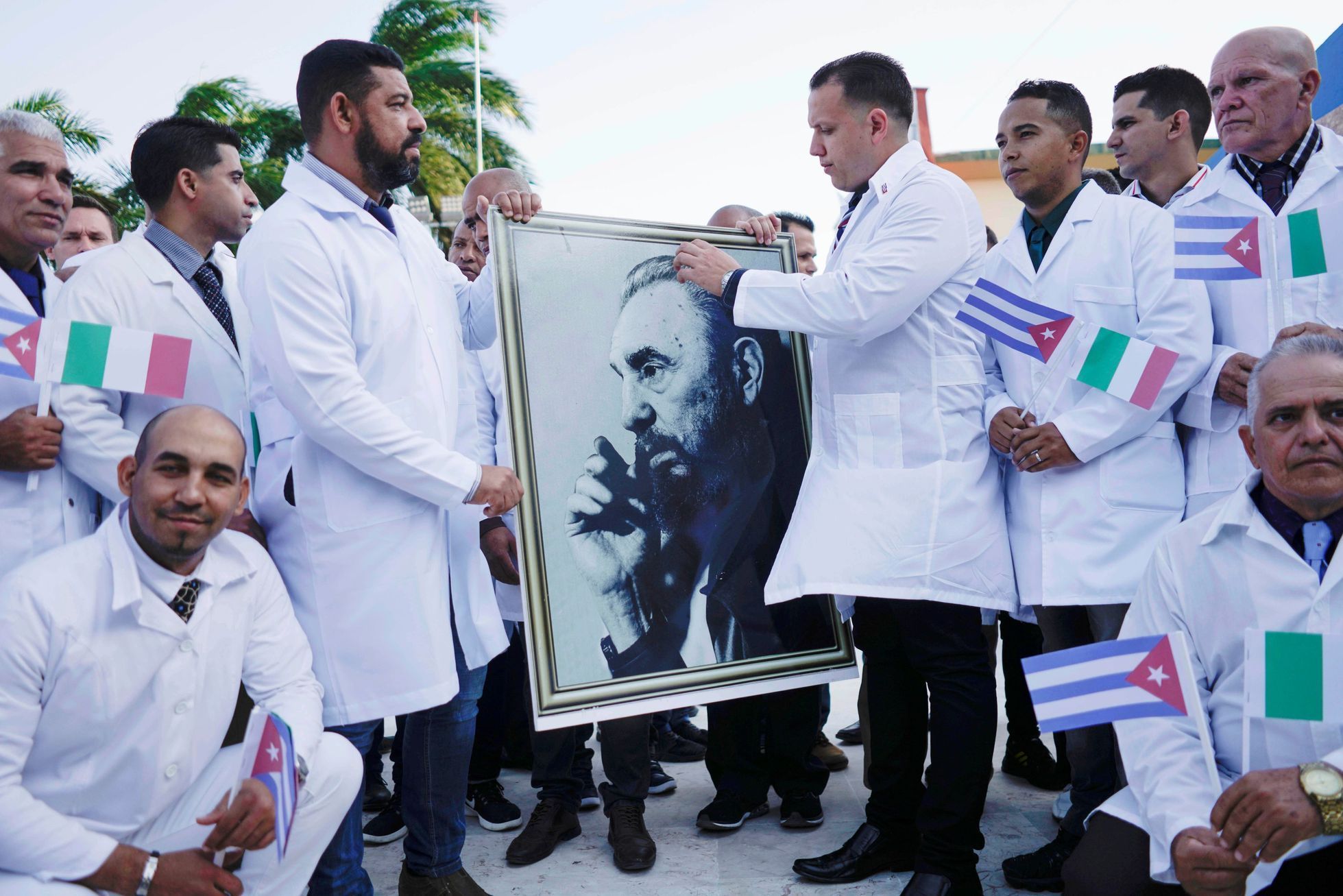 Kubánští doktoři s fotografií Fidela Castra se loučí se veřejností před cestou do Itálie.