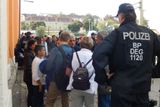 Ve velkých skupinách přijíždějí uprchlíci ve vlacích z Rakouska na nádraží v Pasově. Policisté je drží odděleně od ostatních a později usazují do přistavených autobusů.