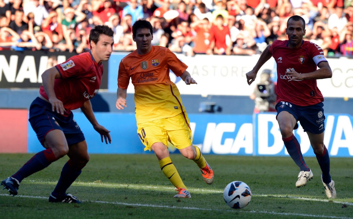 Fotbalista Barcelony Lionel Messi nahrává mezi Marcem Bertanem (vlevo) a Franciscem Punai Martinezem (vpravo) v utkání La Ligy 2012/13 s Osasunou.
