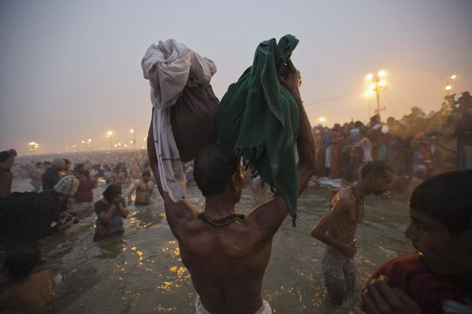 A Hindu devotee holds his belongings aloft as he attends the first "Shahi Snan" (grand bath) at the ongoing "Kumbh Mela", or Pitcher Festival, in the northern Indian city of Allahabad January 14, 2013. Upwards of a million elated Hindu holy men and pilgrims took a bracing plunge in India's sacred Ganges river to wash away lifetimes of sins on Monday, in a raucous start to an ever-growing religious gathering that is already the world's largest. REUTERS/Ahmad Masood (INDIA - Tags: RELIGION SOCIETY TPX IMAGES OF THE DAY) Published: Led. 14, 2013, 8:41 dop.