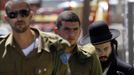 ISRAEL-POLITICS/ Description: An ultra-Orthodox Jewish man walks behind Israeli soldiers at the entrance to a recruiting office in Jerusalem July 4, 2012. Prime Minister Benjamin Netanyahu's largest coalition partner issued a veiled threat on Wednesday to quit the government over a dispute about a bid to amend Israel's compulsory draft policy opposed by the powerful ultra-Orthodox community. REUTERS/Baz Ratner (JERUSALEM - Tags: POLITICS RELIGION) Published: Čec. 4, 2012, 2:48 odp.