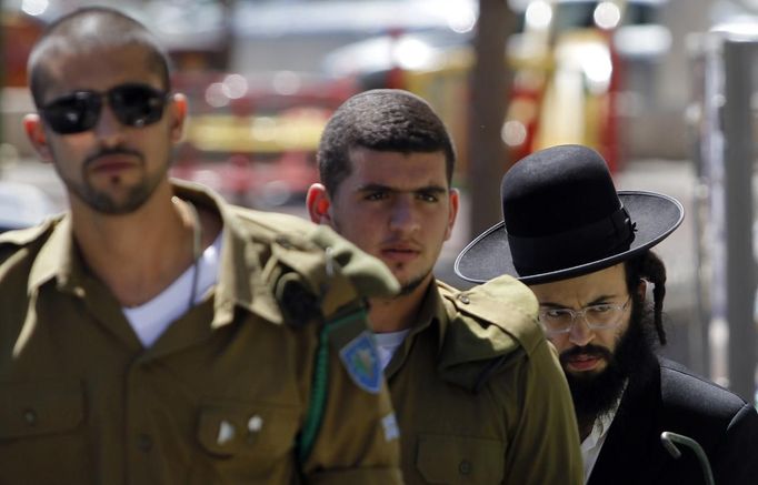 ISRAEL-POLITICS/ Description: An ultra-Orthodox Jewish man walks behind Israeli soldiers at the entrance to a recruiting office in Jerusalem July 4, 2012. Prime Minister Benjamin Netanyahu's largest coalition partner issued a veiled threat on Wednesday to quit the government over a dispute about a bid to amend Israel's compulsory draft policy opposed by the powerful ultra-Orthodox community. REUTERS/Baz Ratner (JERUSALEM - Tags: POLITICS RELIGION) Published: Čec. 4, 2012, 2:48 odp.