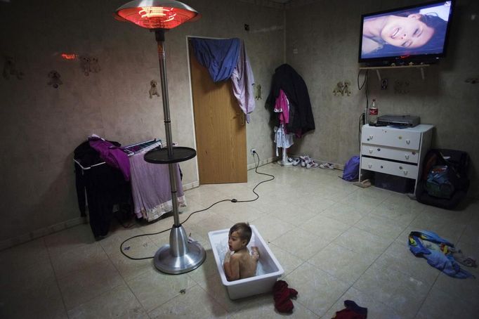 Antonio Gabarri takes a bath as he watches TV at his grandparents' house in the Spanish gypsy settlement of Puerta de Hierro outside Madrid November 24, 2011. Fifty-four families have been living in Puerta de Hierro, on the banks of the Manzanares river for over 50 years. Since the summer of 2010, the community has been subject to evictions on the grounds that the dwellings are illegal. Families whose houses have been demolished, move in with relatives whose houses still remain while the debris keeps piling up around them as more demolitions take place. Picture taken November 24, 2011. REUTERS/Susana Vera (SPAIN - Tags: SOCIETY) ATTENTION EDITORS - PICTURE 18 OF 31 FOR PACKAGE 'GYPSY SITE DEMOLISHED' SEARCH 'GYPSY SITE' FOR ALL IMAGES Published: Lis. 5, 2012, 4:12 odp.