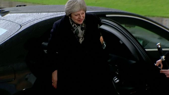 Britská premiérka Theresa Mayová se nemohla dostat z auta. S dveřmi u mercedesu chvíli marně zápasili dva lidé.