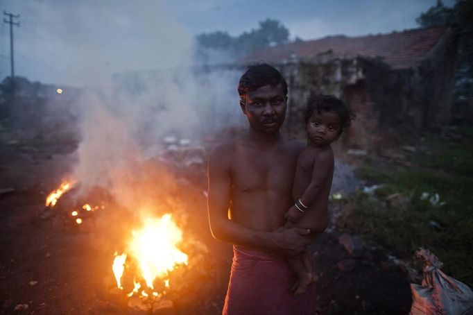 A man holds his child while standing next to burning coal to make it usable for domestic purposes such as for cooking at Dhanbad district in the eastern Indian state of Jharkhand September 19, 2012. With oil and gas output disappointing and hydropower at full throttle, Asia's third-largest economy still relies on coal for most of its vast energy needs. About 75 percent of India's coal demand is met by domestic production and, according to government plans, that won't change over the next five years. Picture taken September 19, 2012. To match INDIA-COAL/ REUTERS/Ahmad Masood (INDIA - Tags: BUSINESS EMPLOYMENT ENERGY SOCIETY ENVIRONMENT) Published: Říj. 21, 2012, 10:18 odp.