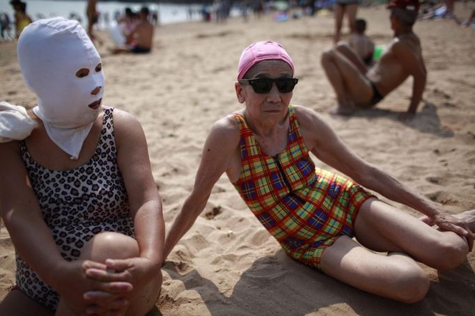 A woman, wearing a nylon mask, rests on the shore during her visit to a beach in Qingdao, Shandong province July 6, 2012. The mask, which was invented by a woman about seven years ago, is used to block the sun's rays. The mask is under mass production and is on sale at local swimwear stores. REUTERS/Aly Song (CHINA - Tags: SOCIETY ENVIRONMENT TRAVEL) Published: Čec. 6, 2012, 4:11 odp.