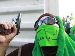 Stoupenkyně Kaddáfího mává na demonstraci pistolí.