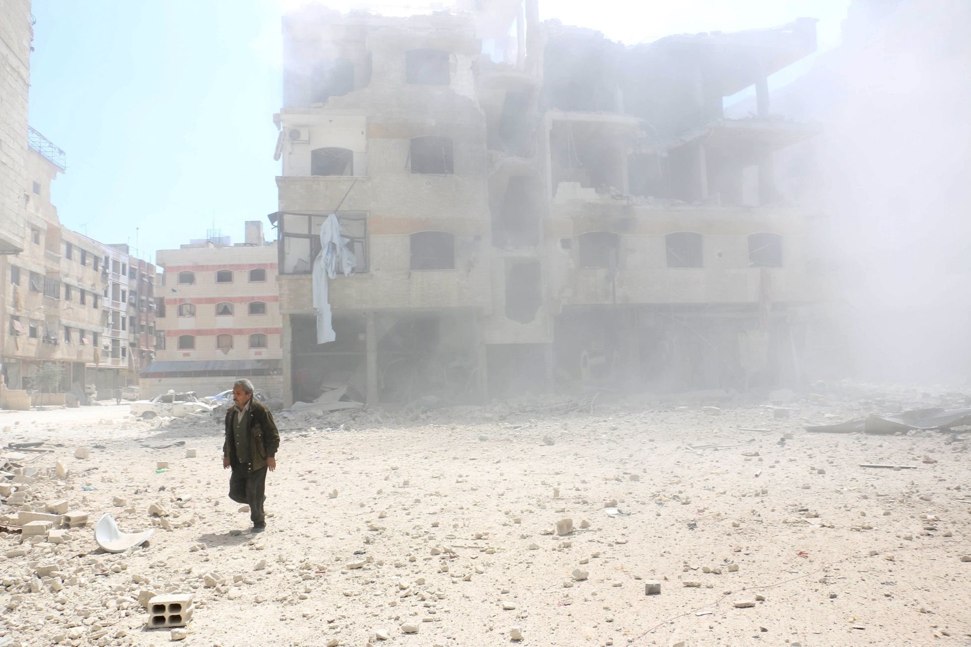 Muž jde kolem bombardované budovy na damašském předměstí Ghúta.