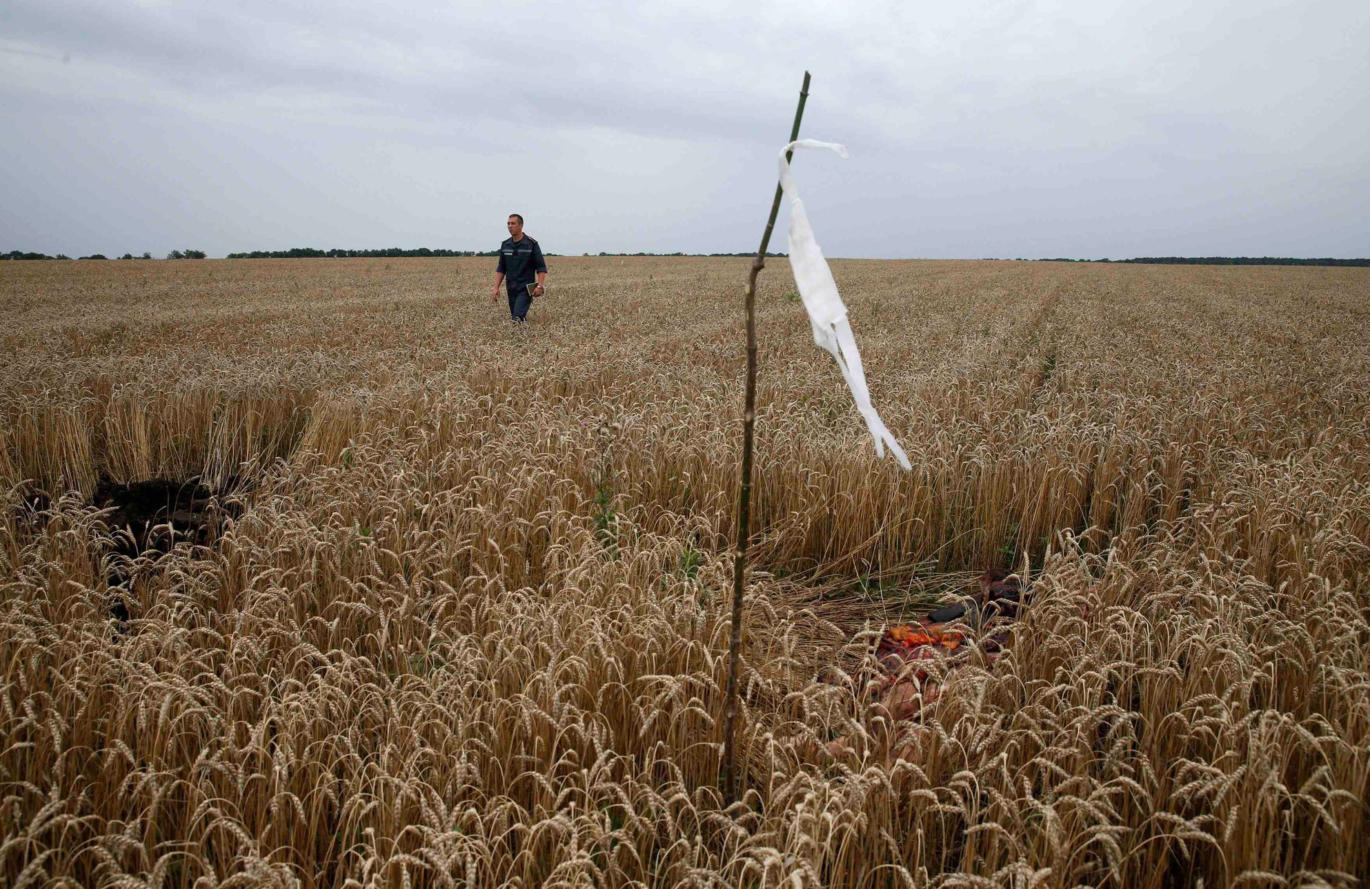 A member of the Ukrainian Emergency Ministry walks past a white flag marking the location of a body, close to the site of Thursday's Malaysia Airlines Boeing 777 plane crash near Grabovo