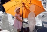Matka pomáhá malé dívce držet deštník nad ledovou sochou vytvořenou z vody ze Žluté řeky, řeky Cháng Jiang a Gangy na výstavě organizace Greenpeace u jednoho z chrámů v Pekingu. (vydražte tento snímek, pomozte dětem - online na www.sanceprodeti.cz )