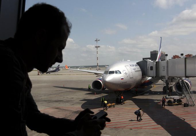 A passenger checks his phone in front of an Aeroflot passenger plane due to depart to Cuba, parked at a terminal of Moscow's Sheremetyevo airport, June 24, 2013. Washington pressed Moscow on Monday to do all in its power to expel former U.S. spy agency contractor Edward Snowden before he gets the chance to take an expected flight to Cuba to evade prosecution in the United States for espionage. REUTERS/Maxim Shemetov (RUSSIA - Tags: POLITICS MEDIA) Published: Čer. 24, 2013, 9:01 dop.