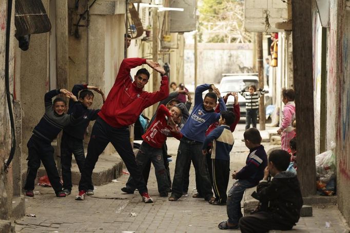 Gaza runner Bahaa al-Farra stretches during a training session as children mimic him while posing for the camera in Shati refugee camp in Gaza City