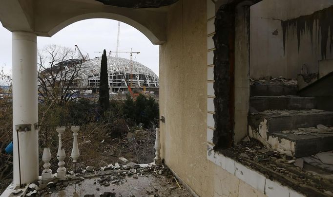 The Olympic stadium for the Sochi 2014 Winter Olympics is seen from a house that has to be torn down as it is within the perimeters of the Olympic Park in Adler, near Sochi February 18, 2013. Although many complexes and venues in the Black Sea resort of Sochi mostly resemble building sites that are still under construction, there is nothing to suggest any concern over readiness. Construction will be completed by August 2013 according to organizers. The Sochi 2014 Winter Olympics opens on February 7, 2014. REUTERS/Kai Pfaffenbach (RUSSIA - Tags: BUSINESS CONSTRUCTION ENVIRONMENT SPORT OLYMPICS) Published: Úno. 18, 2013, 5:42 odp.