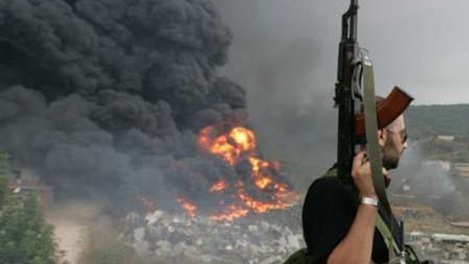 Ozbrojenec hnutí Hizballáh sleduje oheň a kouř stoupající z ostřelovaného objektu na předměstí Bejrútu.