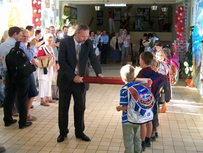 Ředitel ZŠ Šutka Zbyněk Drozda slavnostně pasuje nové žáky. Rodiče přihlížejí.