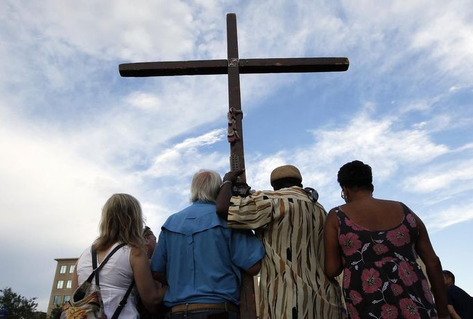 People hold a cross during a vigil for victims behind the theater where a gunman opened fire on moviegoers in Aurora, Colorado July 22, 2012. Residents of a Denver suburb mourned their dead on Sunday from a shooting rampage by a "demonic" gunman who killed 12 people and wounded 58 after opening fire at a cinema showing the new Batman movie. REUTERS/Shannon Stapleton (UNITED STATES - Tags: CRIME LAW) Published: Čec. 23, 2012, 2:29 dop.