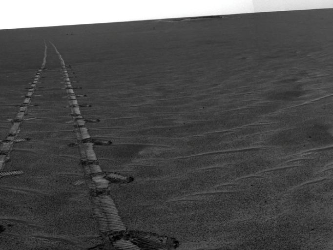 Autonomous Hazard Checks Leave Patterned Rover Tracks on Mars A dance-step pattern is visible in the wheel tracks near the left edge of this scene recorded by the navigation camera on NASA's Mars Exploration Rover Opportunity during the 2,554th Martian day, or sol, of the rover's work on Mars (April 1, 2011). The pattern comes from use of a new technique for Opportunity to autonomously check for hazards in its way while driving backwards. For scale, the distance between the parallel tracks of the left and right wheels is about 1 meter (about 40 inches). The rover team routinely tells Opportunity to drive backwards because experience has shown this is less likely to increase the amount current drawn by the drive motor in the right-front wheel. More than two years ago, the right-front wheel on Opportunity began showing signs of drawing more current than other wheels. Opportunity's twin, Spirit, had shown similar elevated current in the right-front wheel for more than a year before that wheel on Spirit stopped working in 2006. The view looks back after Sol 2554's drive at the tracks imprinted by the drive. The drive covered at total of 118.6 meters (389 feet). Rover drivers had planned the drive based on images taken from the rover's Sol 2553 location. The first portion -- which imprinted the more distant, simpler, tracks -- was a backward "blind" drive. Rover drivers command blind drives -- either forward or backward -- when they can assess the safety of the terrain well enough from the images taken at the drive's starting point that they don't need the rover to pause and look for obstacles along the route. For the Sol 2554 drive over flat ground, the drivers chose a blind drive of 100 meters (328 feet). They commanded Opportunity to begin using backward autonomous navigation after it reached the end of the blind drive on that sol. That "backward autonav" driving imprinted the nearest portion of the tracks visible here. The rover team began using the backward autonav strategy last year as a modification of forward autonav, which the team has used since the rovers' first year on Mars. In autonav mode, the rover pauses periodically during a drive, uses its stereo navigation camera to view the route in the intended drive direction, analyzes the images for potential hazards in the route, and makes a decision about what to do based on that analysis. One catch, when driving backwards, is that the navigation camera's view is partially blocked over the rear of the rover by the low-gain antenna. So, lest a hazard be hidden behind that antenna, the backward autonav technique includes turning the rover 17.5 degrees away from the drive direction just before taking the navigation camera images. This gives the camera an unobstructed view in the drive direction. This little maneuver -- repeated every 1.2 meters -- is what created the dance-step pattern in the foreground portion of the rover tracks in this image. In forward autonav, Opportunity can plot its own way around an obstacle and continue driving. In backward autonav, Opportunity just ends the drive for the day if the onboard analysis of images detects a hazard in the route. On the level terrain Opportunity has been crossing this spring on the trek from Santa Maria crater toward Endeavour crater, obstacles are few, so backward autonav has significantly extended the distance the rover can cover in one sol's driving. This mosaic combining several pointings of the navigation camera is presented in a cylindrical projection. The center of the image is toward the northeast, and the full view covers a sweep of 252 degrees, from westward on the left to southeastward on the right. Opportunity has been exploring the Meridiani Planum region of Mars since early 2004 in a mission originally planned to last for three months. Both Opportunity and Spirit have made important discoveries about wet environments on ancient Mars that may have been favorable for supporting microbial life. NASA's Jet Propulsion Laboratory, a division of the California Institute of Technology in Pasadena, manages the Mars Exploration Rover Project for NASA's Science Mission Directorate, Washington. Image credit: NASA/JPL-Caltech