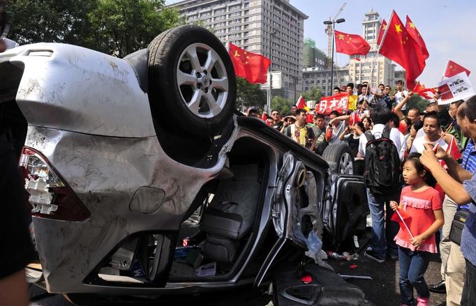 Demonstrators hold Chinese flags and banners beside an overturned car of a Japanese brand during a protest in Xi'an, Shaanxi province September 15, 2012. Thousands of Chinese besieged the Japanese embassy in Beijing on Saturday, hurling rocks, eggs and bottles with protests reported in other major cities in China amid growing tension between Asia's two biggest economies over a group of disputed islands. REUTERS/Rooney Chen (CHINA - Tags: POLITICS) CHINA OUT. NO COMMERCIAL OR EDITORIAL SALES IN CHINA