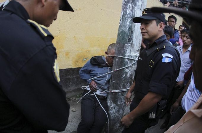 Police officers stand next on a man who is tied up and beaten by villagers, after he was accused of theft, at Tactic, in Alta Verapaz region, about 189km (117 miles) from Guatemala City, September 13, 2012. The local community tied up and beat four men who were accused of theft in the aftermath of a school killing, which had occurred on Wednesday. The man, who had entered a classroom and killed two children, ages 8 and 13, with a machete, was lynched and burnt alive by a mob, local media reported. REUTERS/Jorge Dan Lopez (GUATEMALA - Tags: CRIME LAW SOCIETY) Published: Zář. 13, 2012, 6:15 odp.