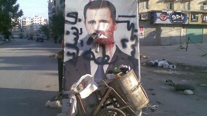 A defaced poster of Syria's President Bashar al-Assad is seen near garbage containers in Aleppo July 24, 2012. The words on the poster read, "We coming, duck ass". Picture taken July 24, 2012. REUTERS/Shaam News Network/Handout (SYRIA - Tags: POLITICS CIVIL UNREST) FOR EDITORIAL USE ONLY. NOT FOR SALE FOR MARKETING OR ADVERTISING CAMPAIGNS. THIS IMAGE HAS BEEN SUPPLIED BY A THIRD PARTY. IT IS DISTRIBUTED, EXACTLY AS RECEIVED BY REUTERS, AS A SERVICE TO CLIENTS Published: Čec. 25, 2012, 9:41 dop.