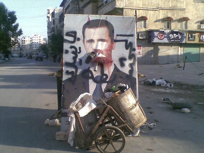 A defaced poster of Syria's President Bashar al-Assad is seen near garbage containers in Aleppo July 24, 2012. The words on the poster read, "We coming, duck ass". Picture taken July 24, 2012. REUTERS/Shaam News Network/Handout (SYRIA - Tags: POLITICS CIVIL UNREST) FOR EDITORIAL USE ONLY. NOT FOR SALE FOR MARKETING OR ADVERTISING CAMPAIGNS. THIS IMAGE HAS BEEN SUPPLIED BY A THIRD PARTY. IT IS DISTRIBUTED, EXACTLY AS RECEIVED BY REUTERS, AS A SERVICE TO CLIENTS Published: Čec. 25, 2012, 9:41 dop.