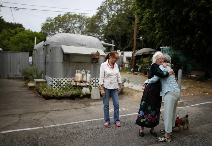 Mary Herring (C), 78, hugs a neighbor as Gayle Cooper (L), 66, looks on in Village Trailer Park in Santa Monica, California July 12, 2012. Developer Marc Luzzatto wants to relocate residents from the trailer park to make way for nearly 500 residences, office space, stores, cafes and yoga studios, close to where a light rail line is being built to connect downtown Los Angeles to the ocean. Village Trailer Park was built in 1951, and 90 percent of its residents are elderly, disabled or both, according to the Legal Aid Society. Many have lived there for decades in old trailers which they bought. The property is valued at as much as $30 million, according the LA Times. Picture taken July 12, 2012. REUTERS/Lucy Nicholson (UNITED STATES - Tags: POLITICS REAL ESTATE BUSINESS SOCIETY TPX IMAGES OF THE DAY) Published: Čec. 14, 2012, 6:54 dop.